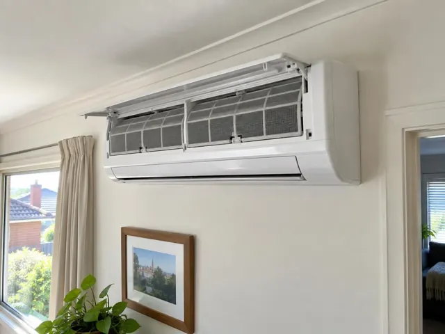 Clean split-system air conditioner with open front panel and visible filters on a cream wall in a home interior in Mile End