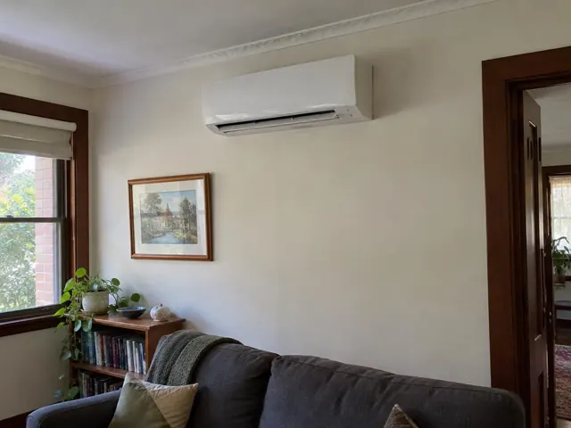 Wall-mounted split system above a lounge in a beige living room with timber trim in Plympton